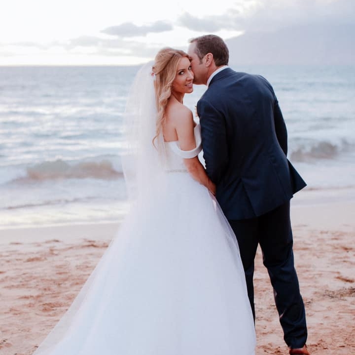 A bride and groom kissing on the beach.