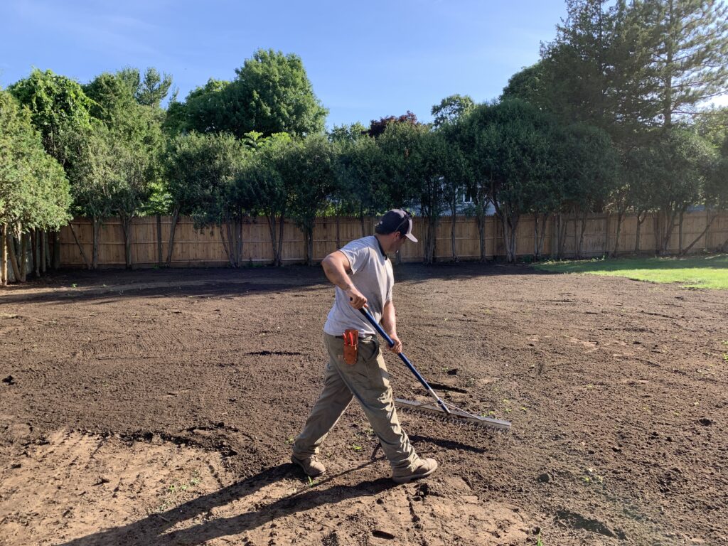 A man using a shovel to dig up dirt in a backyard.