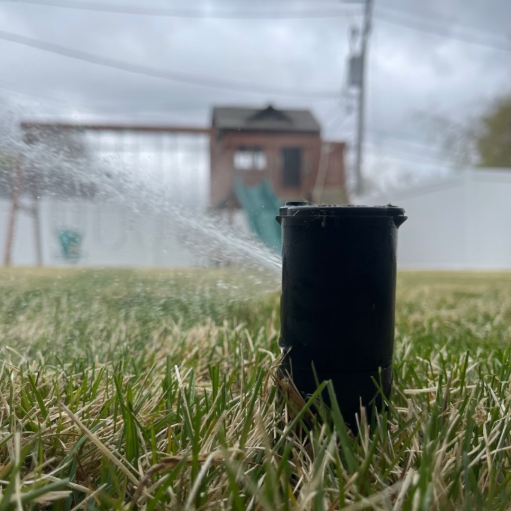 A black sprinkler in the grass next to a playground.