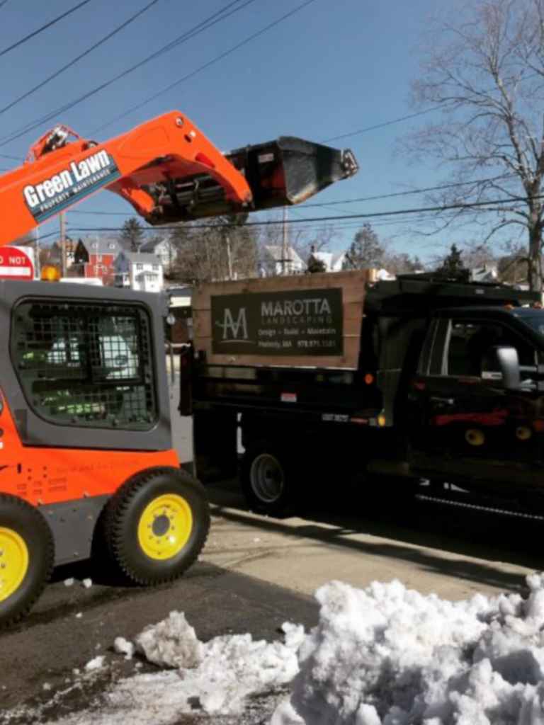 A skid loader is being used to load a truck full of snow.